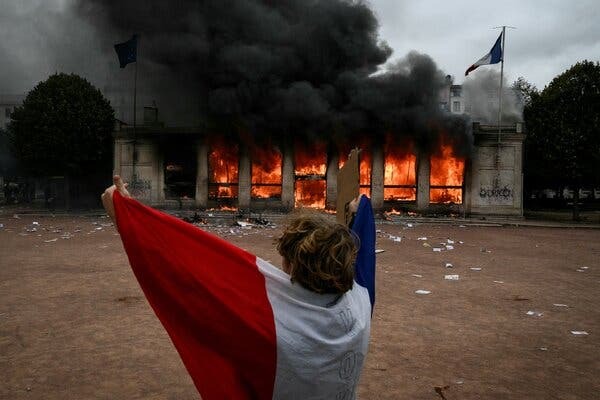 A protester holding a French flag watches a historic building burn during the France protests